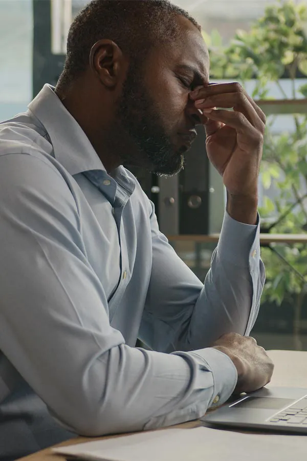 Chronic-Fatigue-Treatment A black man rubbing the top of his nose at his desk, in need of chronic fatigue treatment from Optimal Wellness Medical Group in Grand Rapids.