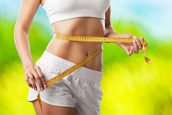 Coolsculpting-Body-Contouring-Clinic Close up of a woman in white sportswear, wrapping a measuring tape around her midsection. Receive CoolSculpting treatment by Optimal Wellness Medical Group in Grand Rapids.