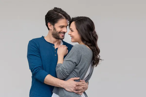 Erectile-Dysfunction-Doctor A man in a blue shirt embracing a woman in a gray shirt smiles due to his successful erectile dysfunction care from Optimal Wellness Medical Group in Grand Rapids.