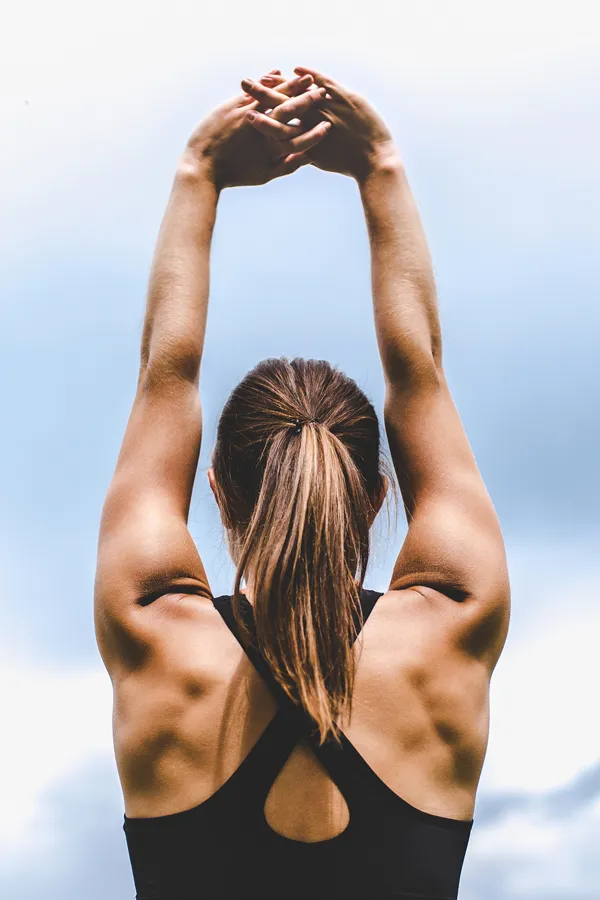 GLP-1-Weight-Loss-Injections-Treatment A toned woman seen from behind stretching her arms into the air. Get GLP-1 Weight Loss Injections from Optimal Wellness Medical Group in Grand Rapids.