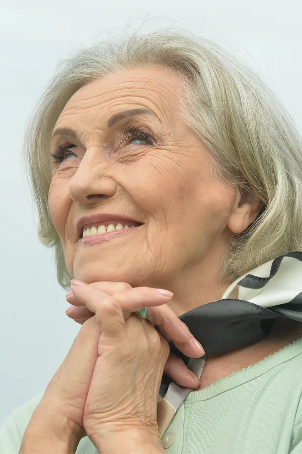 Hot-Flashes-and-Night-Sweats-Treatments An older woman holds her hands together under her chin and looks up at a cool sky smiling. Get treatment for hot flashes and night sweats from Optimal Wellness Medical Group in Grand Rapids.