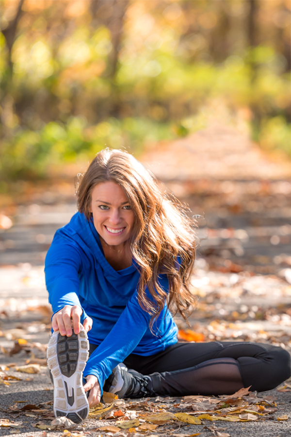 Woman wearing athletic gear stetching on a leaf covered trail during day time. Schedule an InBody Composition Scan with Optimal Wellness Medical Group in Grand Rapids.