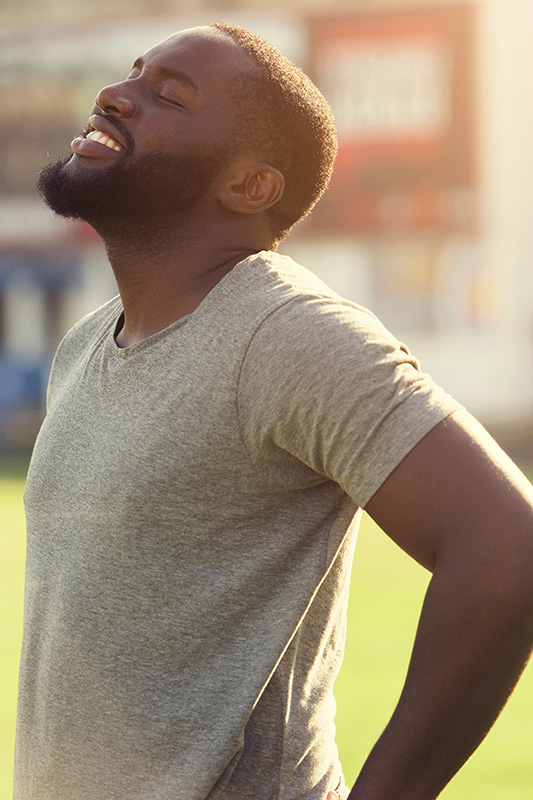 Lean-Muscle-and-Recovery-Treatment A black man in a gray t-shirt and smiles, looking up with closed eyes after a satisfying workout. Get treatment for lean muscle loss and recovery from Optimal Wellness Medical Group in Grand Rapids.