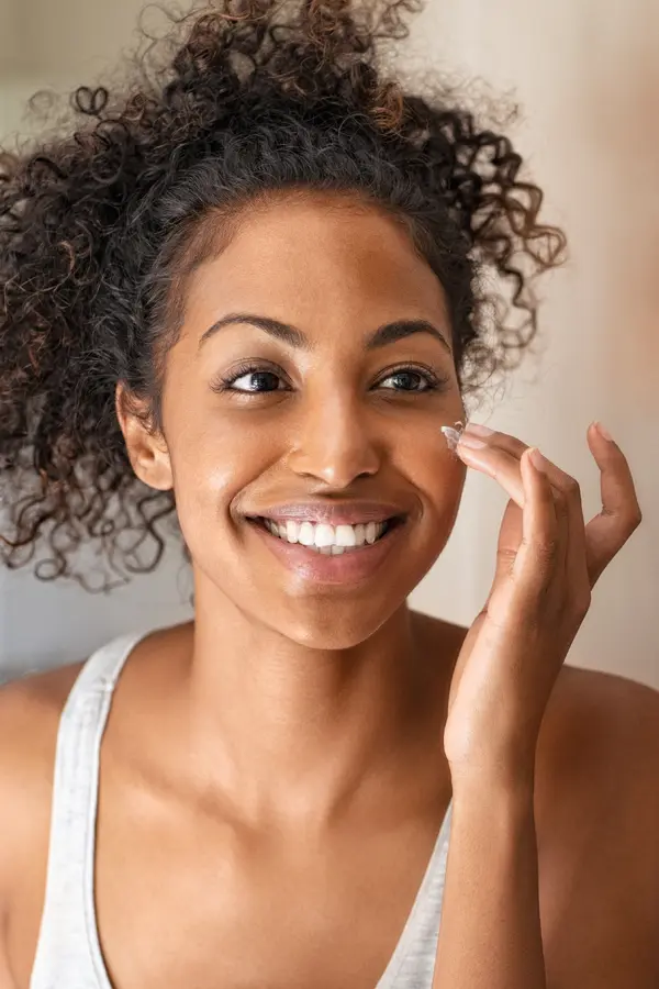 Microneedling-Treatment-2 A black woman smiles and applies skin cream. Get microneedling from Optimal Wellness Medical Group in Grand Rapids.