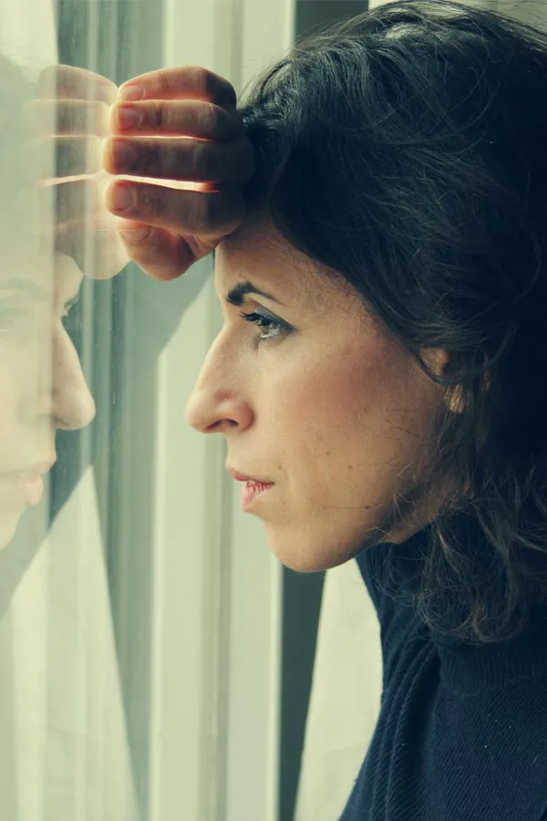 PMOS-Treatment A brunette woman in a thin dark turtleneck looks out the window with a serious expression, suffering from PMOS. Get treatment for Polyendocrine Metabolic Ovarian Syndrome/PMOS from Optimal Wellness Medical Group in Grand Rapids.