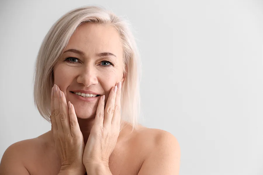 PRP-Microneedling-Clinic A mature woman touches her faces to feel the successful results of PRP microneedling and skin rejuvenation treatments from Optimal Wellness Medical Group in Grand Rapids.