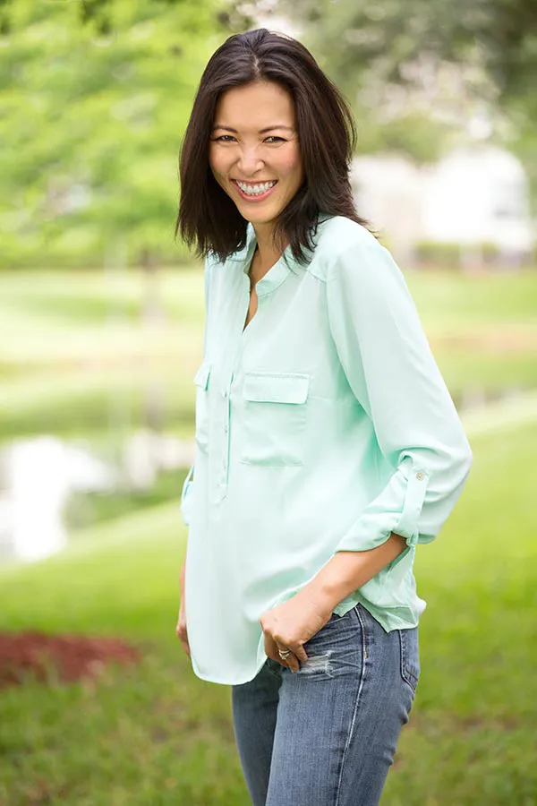 Perimenopause-Treatment A middle-aged brunette woman in a light green button-up shirt stands outside smiling, happy with her perimenopause treatment from Optimal Wellness Medical Group in Grand Rapids.