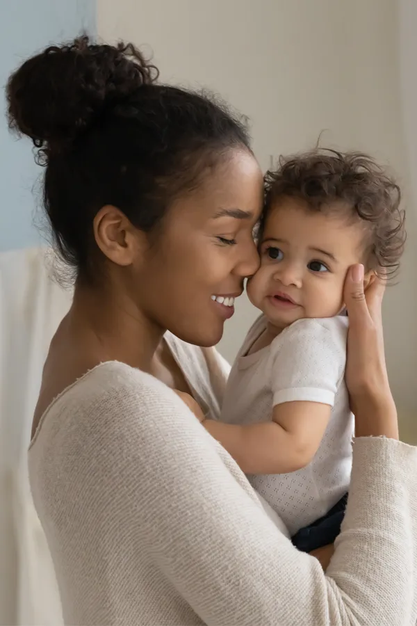 Postpartum-Hormone-Imbalance-Treatment A black woman happily touches her forehead to her infant's head. Get treatment for postpartum hormone imbalance from Optimal Wellness Medical Group in Grand Rapids.